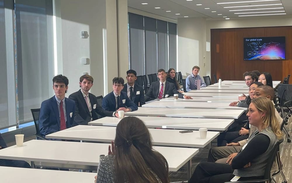 SCG members in business attire seated along a long conference table in a bright office during the EY site visit.