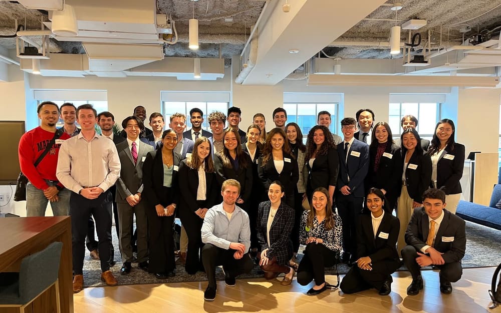 A large group of SCG members in business attire, with name tags, gathered in an open-plan office.