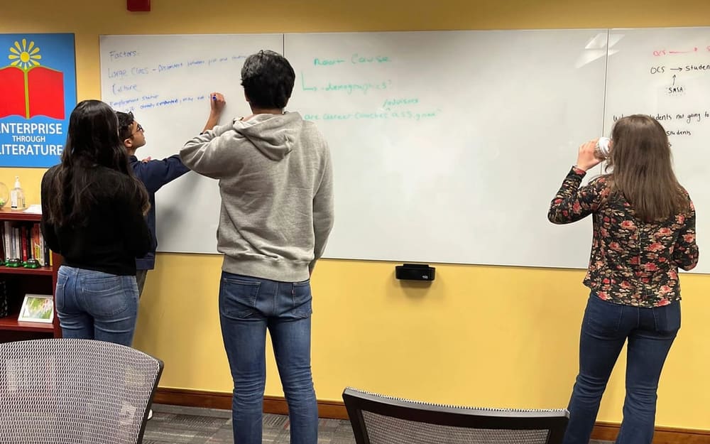 Three members writing ideas on a large whiteboard in a meeting room.