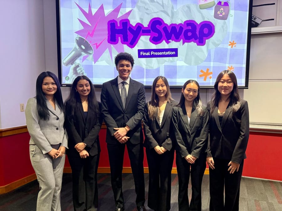 Six students in business attire standing together in front of a screen showing the title slide “Hy-Swap: Final Presentation”.