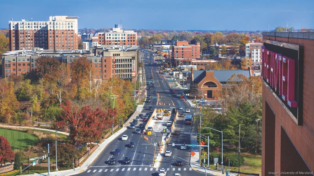 Aerial view of a busy four-lane road through College Park, lined with apartment buildings, shops and autumn trees.