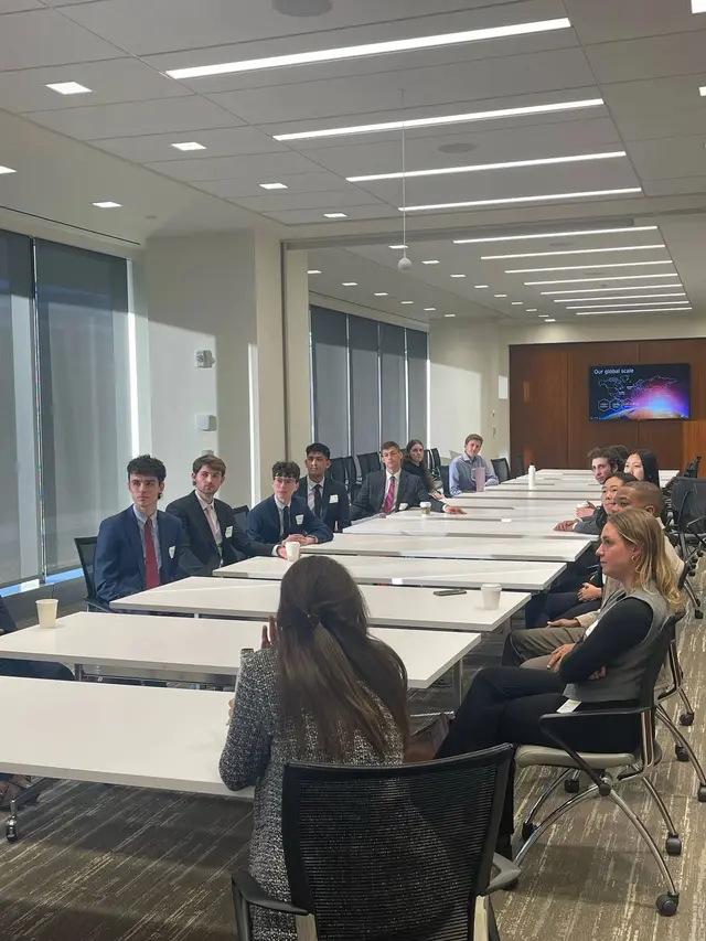 SCG members in business attire seated along a long conference table in a bright office during a site visit to EY.