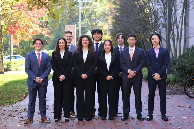 SCG members in business attire standing in two rows on a brick path under autumn trees.