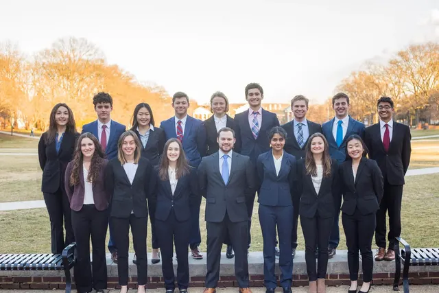 SCG members in suits standing in two rows on a campus lawn in warm evening light.