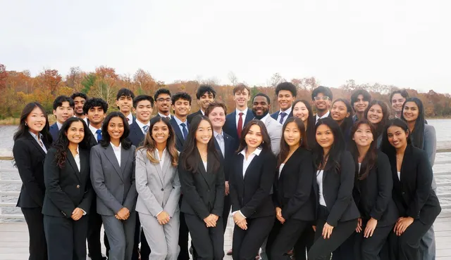 SCG members in suits posing together on a lakeside boardwalk, with autumn trees across the water.