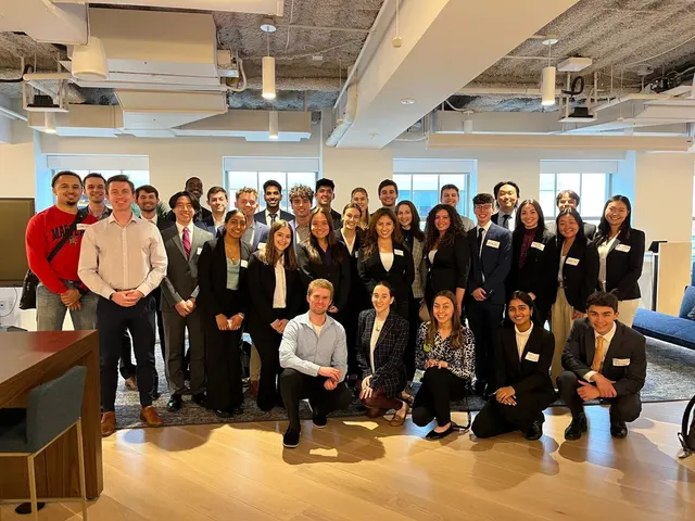A large group of SCG members in business attire with name tags in an open-plan office.