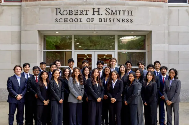 About forty SCG members in business attire standing together in front of the Robert H. Smith School of Business entrance.