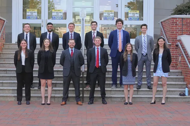 SCG members in business attire standing in two rows on the steps of a brick and glass campus building.