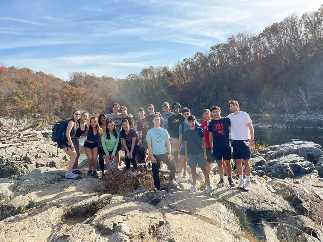 A group of SCG members in casual clothes standing on large rocks above a river on a sunny autumn hike.