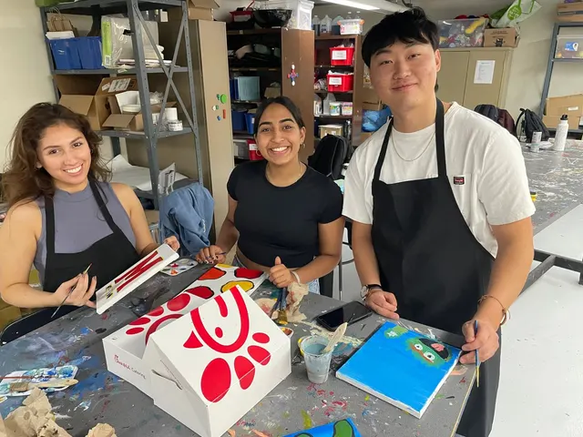 Three members in aprons smiling at the camera while painting at a social.