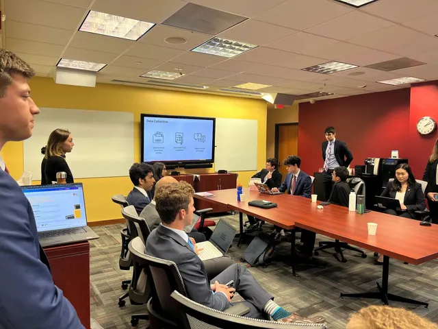 Members in business attire with laptops around a conference table while a slide titled Data Collection is shown on a screen.