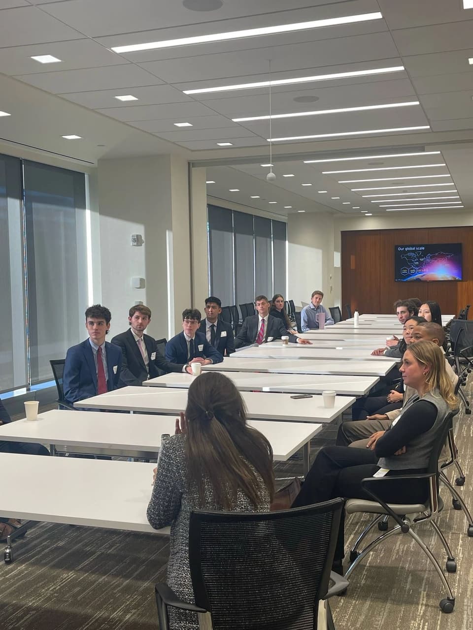 SCG members in business attire seated along a long conference table in a bright office during a site visit to EY.