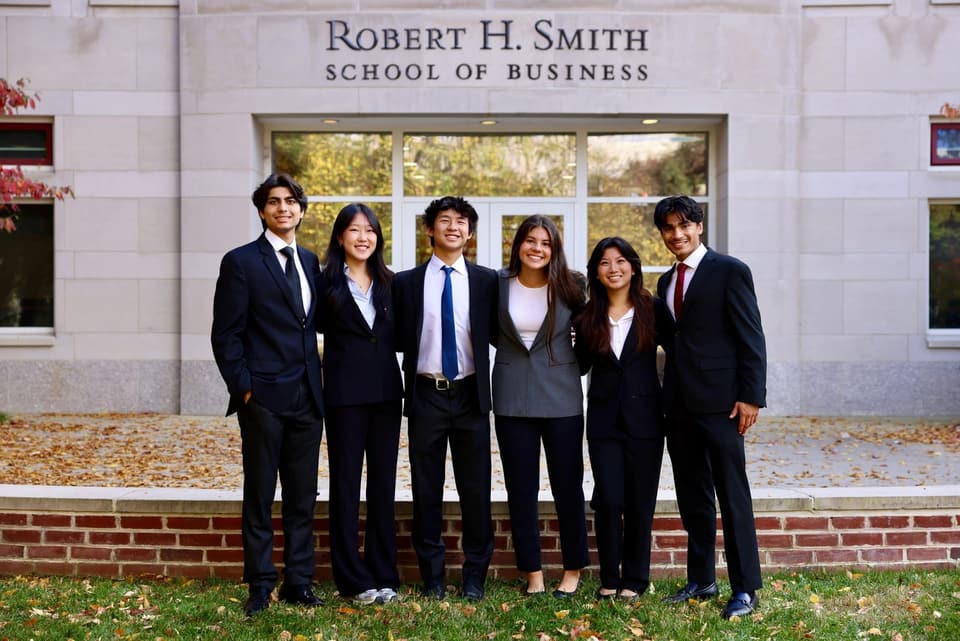 Six members in business attire standing in front of the Robert H. Smith School of Business entrance.