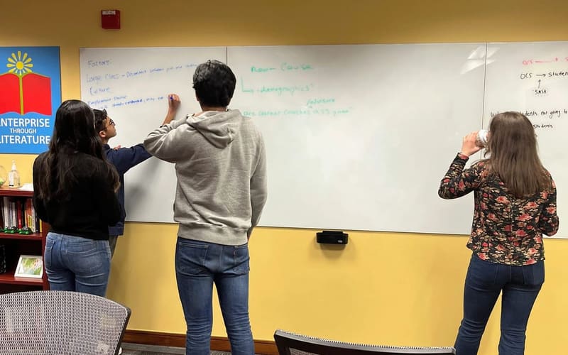 Three members writing ideas on a large whiteboard in a meeting room.