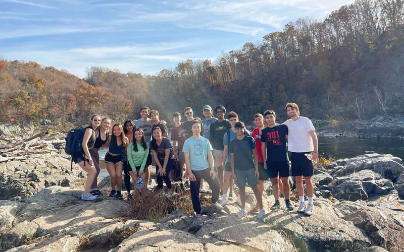 A group of SCG members in casual clothes standing on large rocks above a river on a sunny autumn hike.