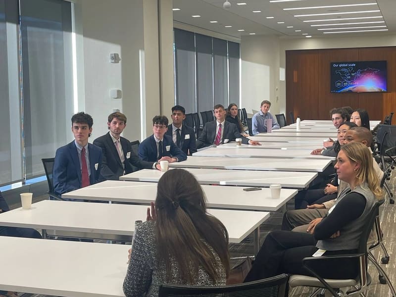 SCG members in business attire seated along a long conference table in a bright office during the EY site visit.