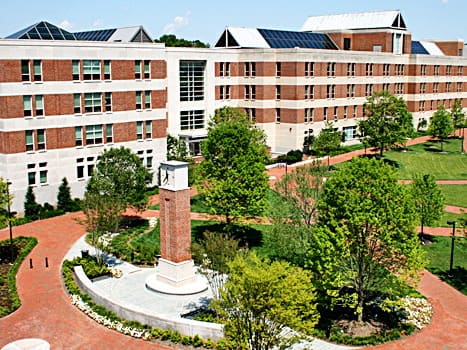 A large brick and white campus building seen from above, with green lawns, brick paths and a brick clock tower in front.