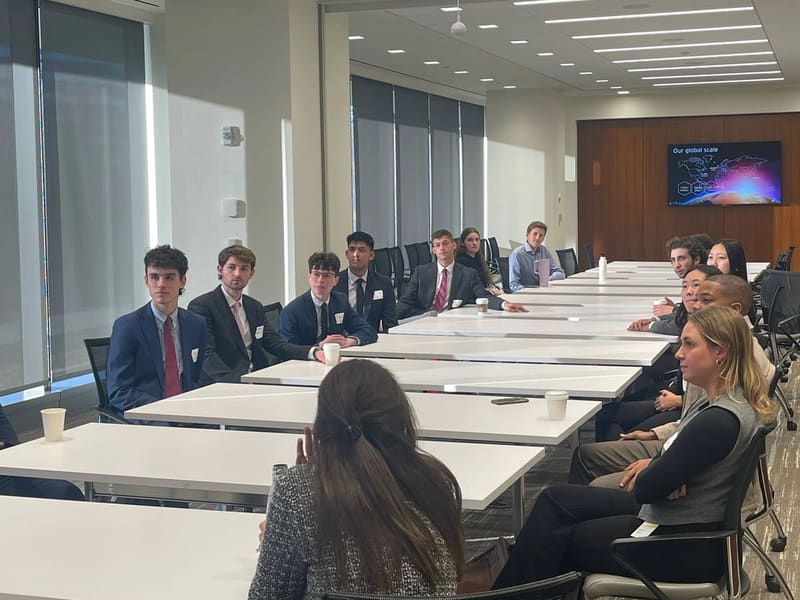 SCG members in business attire seated along a long conference table in a bright office during the EY site visit.