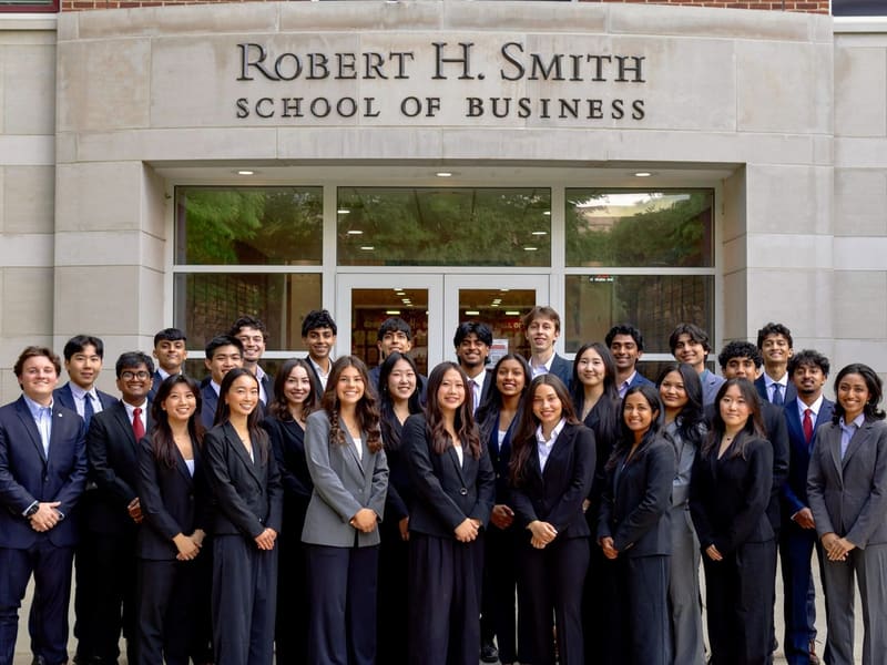 About forty SCG members in business attire standing together in front of the Robert H. Smith School of Business entrance.