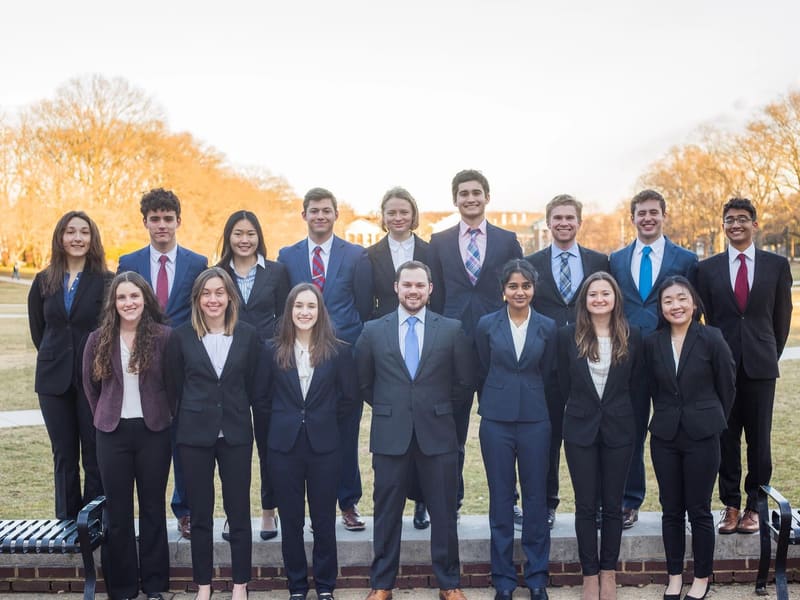 SCG members in suits standing in two rows on a campus lawn in warm evening light.